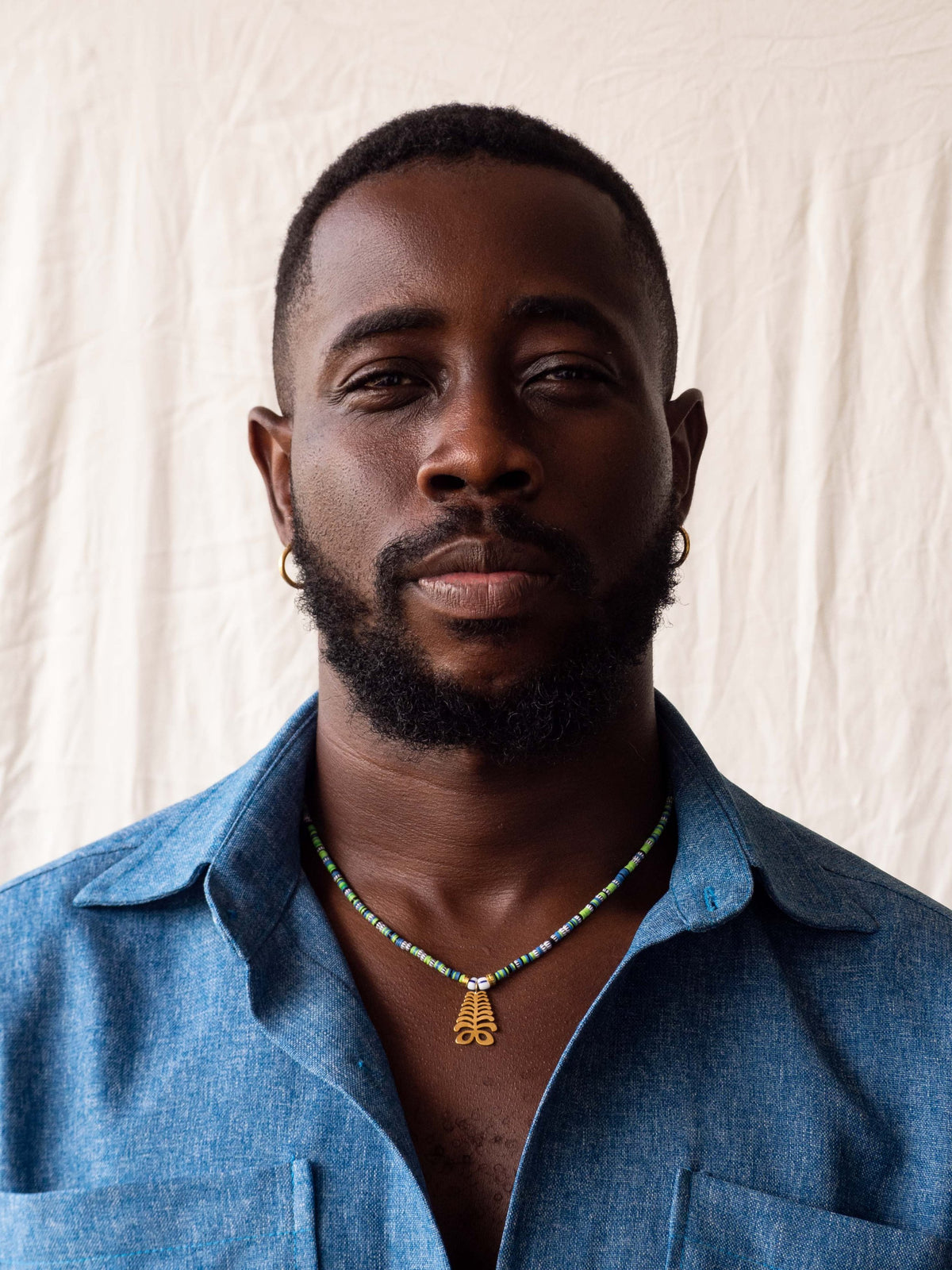 Statement necklace with colorful Ghanaian glass beads and gold-plated brass Adinkra amulets, representing African heritage.
